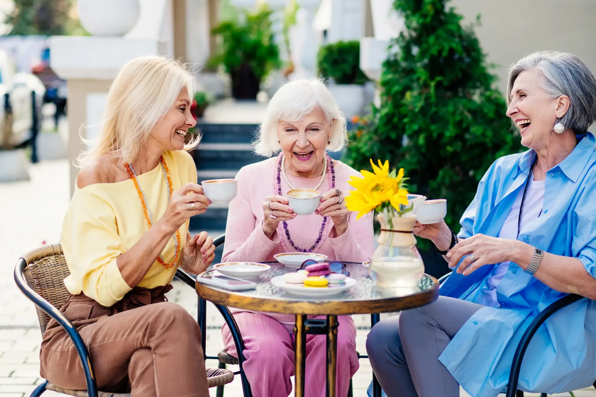 Three senior women enjoying tea and macarons at an outdoor café